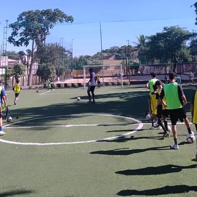Alunos com coletes em treino no campo de grama sintética da academia