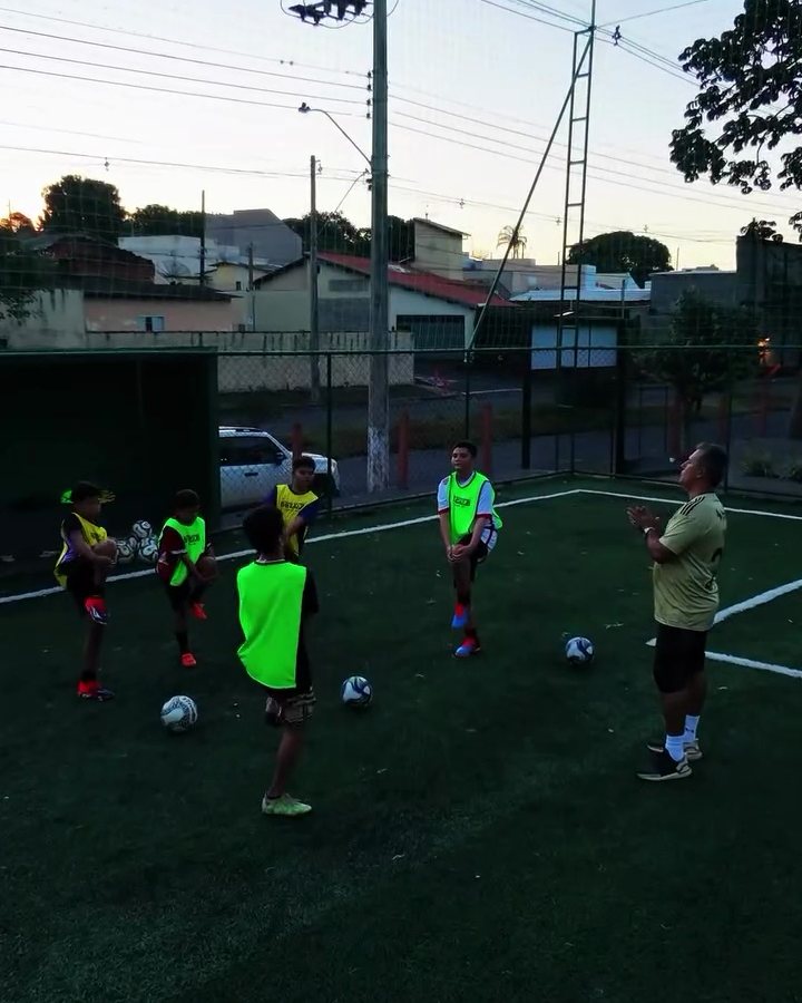 Crianças com coletes e bolas em treino conduzido pelo professor no campo da academia