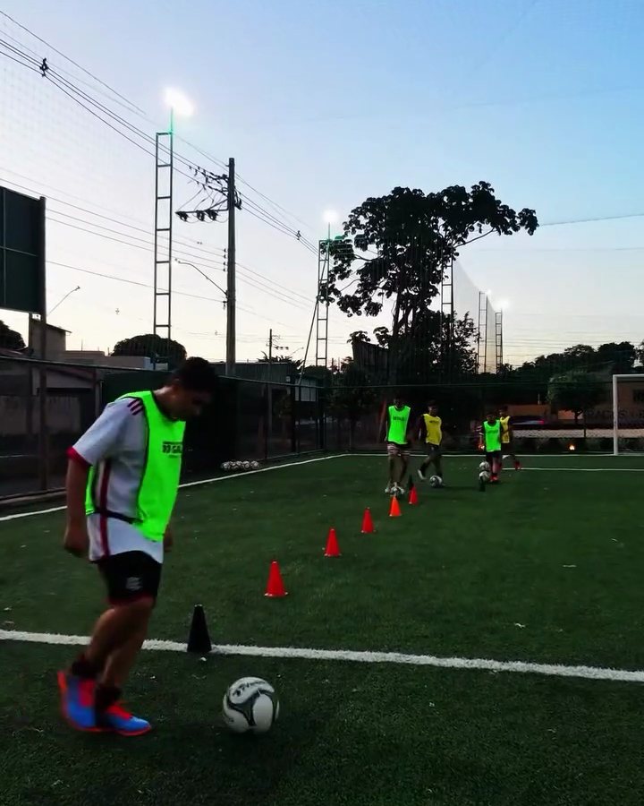 Aluno conduzindo a bola entre cones em treino de fundamento